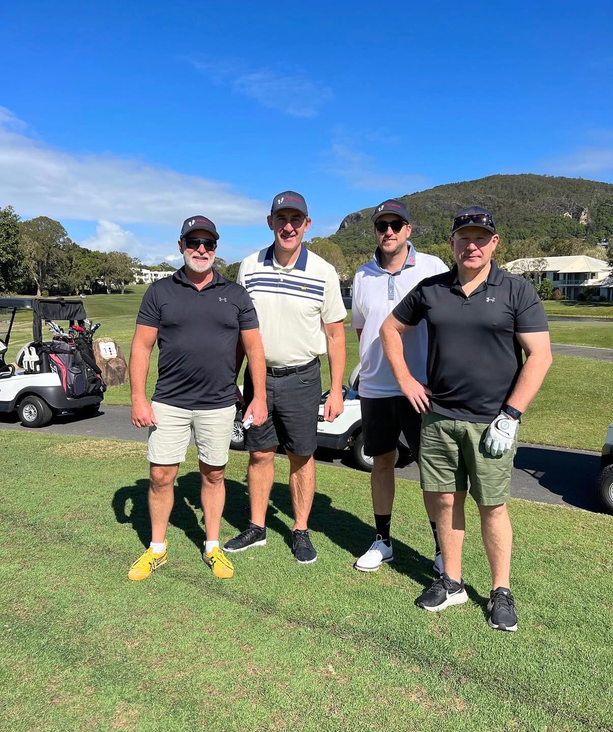 Players beside golf carts with the course and hills behind